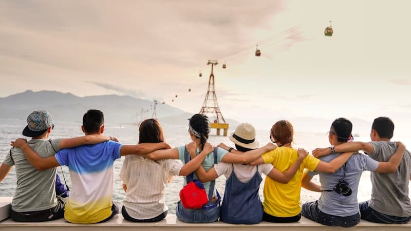 Eight friends arm in arm on a seawall at dusk